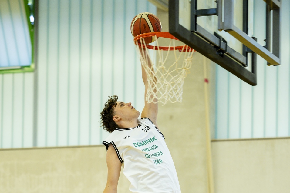 Ein Jugendlicher springt zum Dunking mit einem Basketball &uuml;ber den Korb in einer Sporthalle.