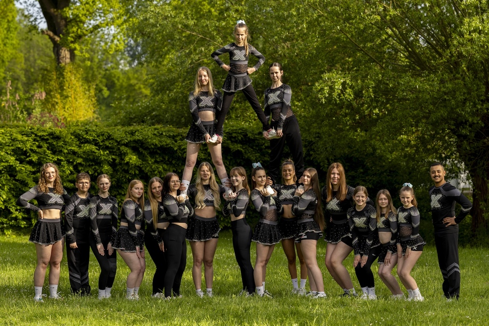 Gruppe von Cheerleadern in Uniformen steht im Freien, einige sind in akrobatischen Posen aufeinander gestapelt.