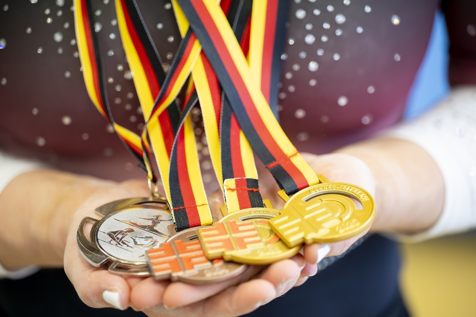 Nahaufnahme einer Hand, die mehrere Medaillen in Silber und Gold mit schwarz-rot-goldenen B&auml;ndern h&auml;lt.