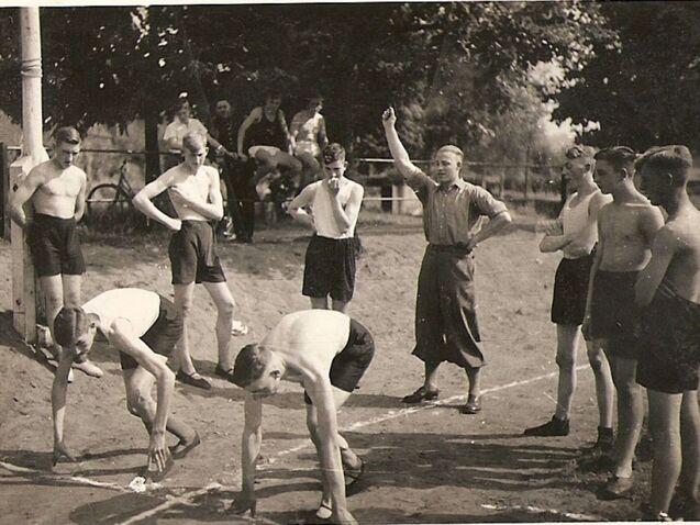 Gruppe von Jungen in der Startposition für ein Rennen, umgeben von Zuschauern, an einem sonnigen Tag im Freien.