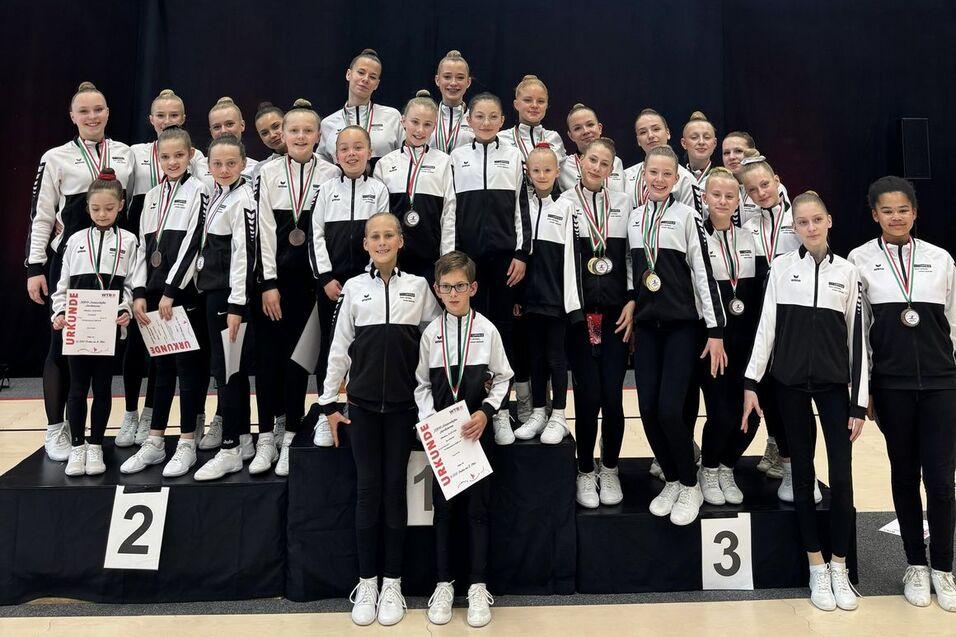 Gruppenschüler im Sportanzug stehen auf einem Podium, tragen Medaillen und halten Urkunden in den Händen.