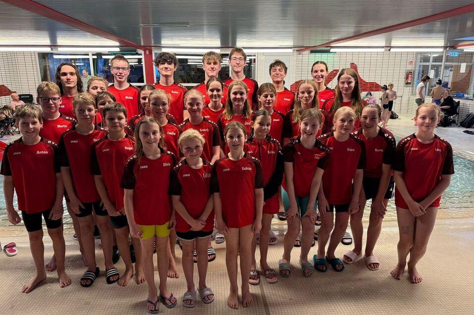 Gruppenfoto von Schwimmern in roten Trikots, aufgeteilt in zwei Reihen vor einem Schwimmbad.