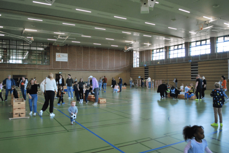 Vielseitige Sport- und Spielveranstaltung in einer Halle mit Kindern und Erwachsenen, die sich aktiv beteiligen.