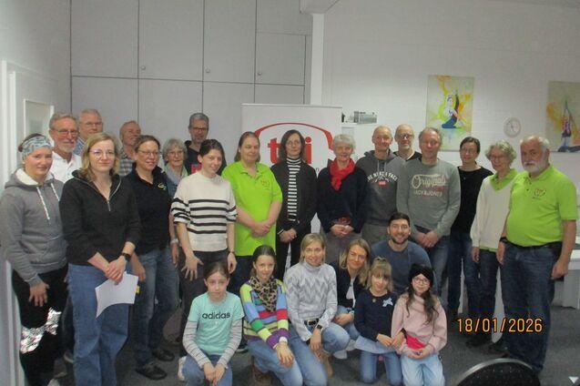 Gruppenfoto von 29 Personen, die in einem Raum posieren, einige tragen grüne Shirts, mit einem Banner im Hintergrund.
