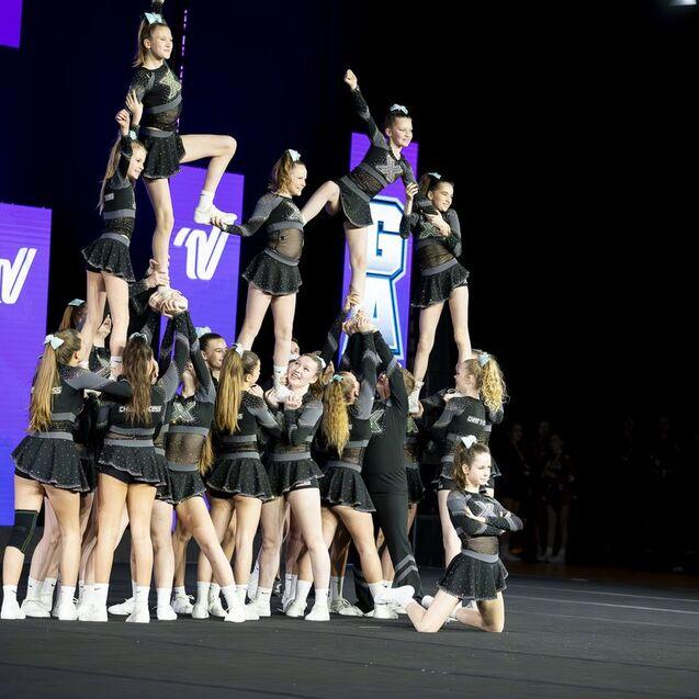 Gruppenchoreografie mit Cheerleadern, die eine Pyramide bilden, während andere sie anfeuern, vor einem leuchtenden Hintergrund.