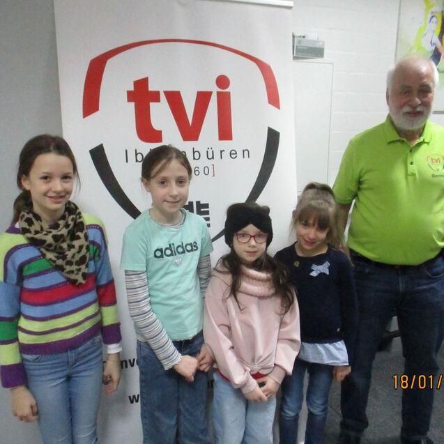 Viere Mädchen und ein Mann stehen vor einem Banner mit „tvi“ in einem Raum. Alle lächeln freundlich in die Kamera.