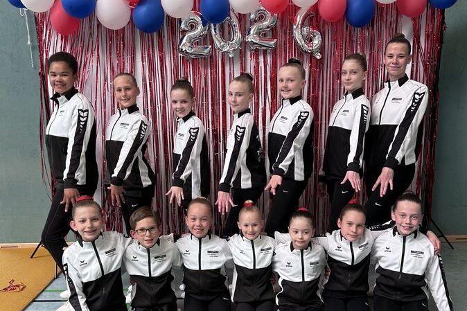 Gruppe von Tänzerinnen in Sportanzügen vor einer Dekoration mit Luftballons und einem aufgestellten „2026“.