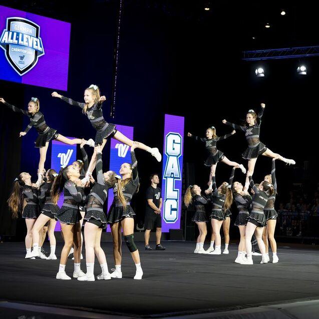 Gruppenchoreografie mit Cheerleadern in schwarz, die Akrobatik und Stunts auf einer B&uuml;hne ausf&uuml;hren.
