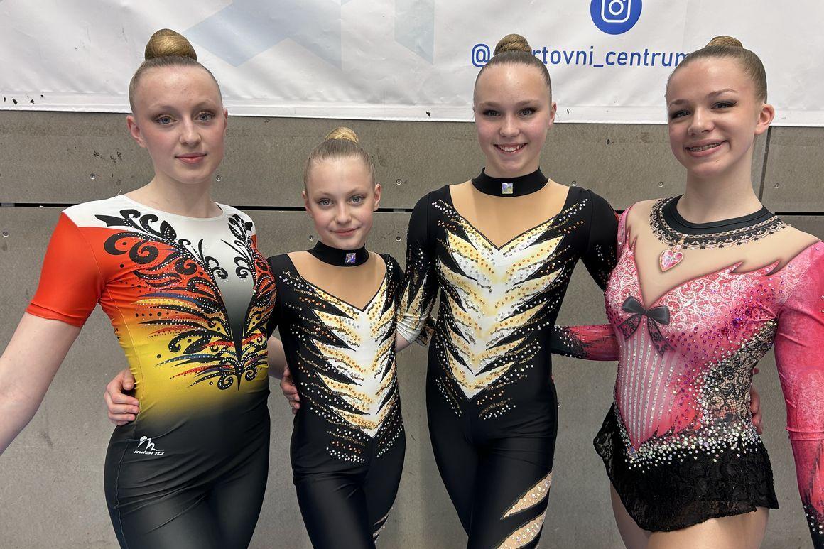 Vier weibliche Sportlerinnen in bunter Gymnastikbekleidung posieren lächelnd nebeneinander vor einer Wand.