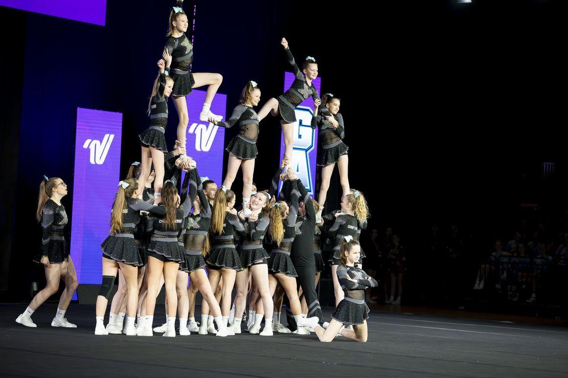 Gruppenchoreografie mit Cheerleadern, die eine Pyramide bilden, während andere sie anfeuern, vor einem leuchtenden Hintergrund.