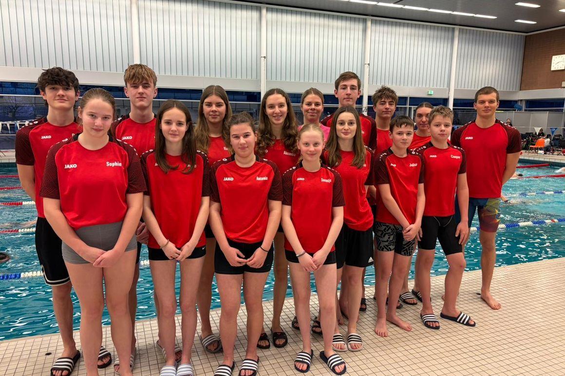 Gruppe von Schwimmern in roten Trikots steht am Beckenrand eines Schwimmbads.