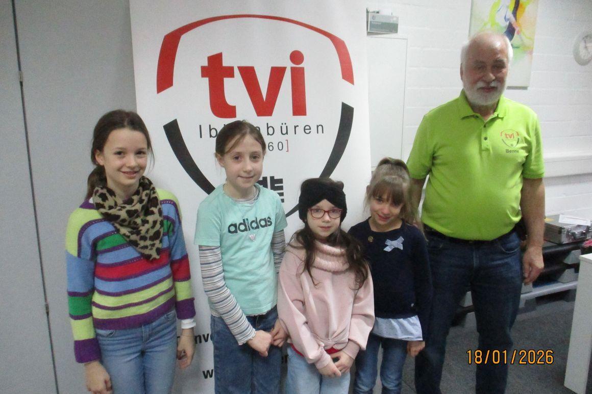 Viere Mädchen und ein Mann stehen vor einem Banner mit „tvi“ in einem Raum. Alle lächeln freundlich in die Kamera.
