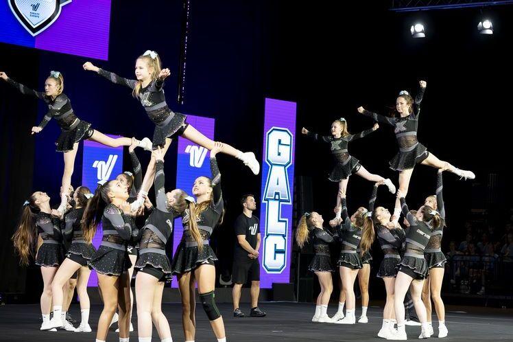 Gruppenchoreografie mit Cheerleadern in schwarz, die Akrobatik und Stunts auf einer B&uuml;hne ausf&uuml;hren.