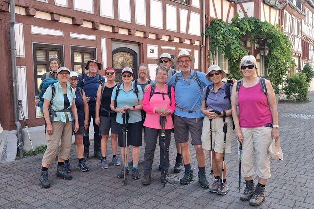 Gruppe von zwölf Wanderern in Outdoor-Bekleidung posiert vor einem historischen Fachwerkhaus in der Stadt.