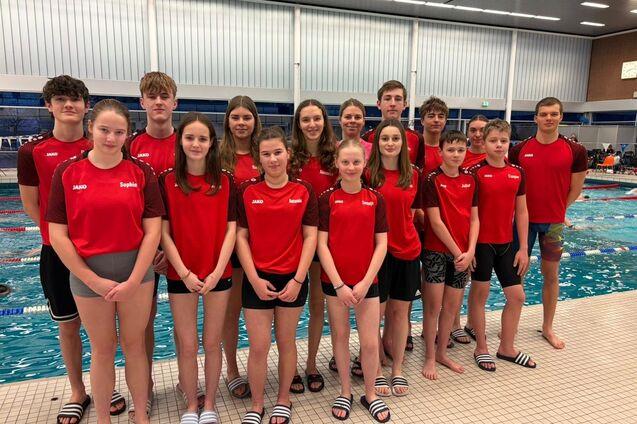 Gruppe von Schwimmern in roten Trikots steht am Beckenrand eines Schwimmbads.