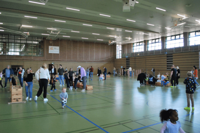 Vielseitige Sport- und Spielveranstaltung in einer Halle mit Kindern und Erwachsenen, die sich aktiv beteiligen.