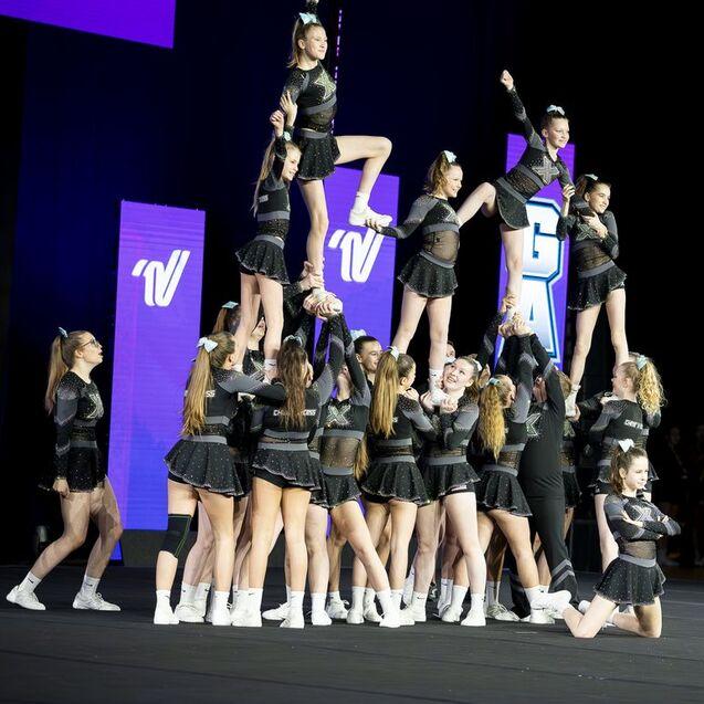 Gruppenchoreografie mit Cheerleadern, die eine Pyramide bilden, w&auml;hrend andere sie anfeuern, vor einem leuchtenden Hintergrund.