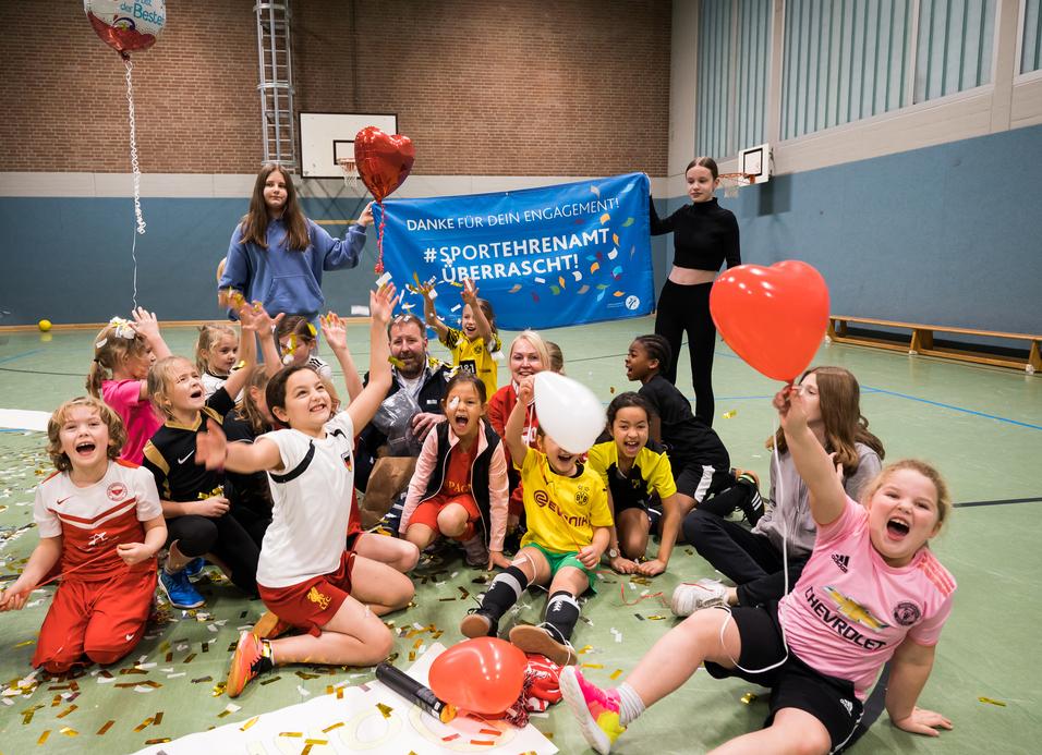 Gruppenszenen mit begeisterten Kindern in Sportkleidung, die Ballons halten und vor einem Danke-Schild feiern.