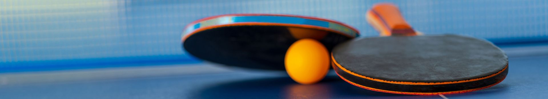Zwei Tischtennisschläger und ein Ball liegen vor dem Netz auf einer Tischtennisplatte.